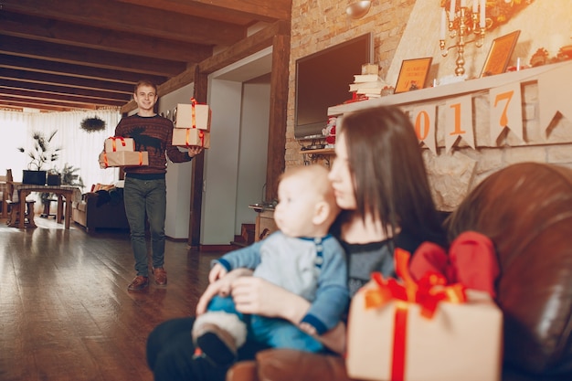 Man carrying gifts while his wife is sitting with a baby on a sofa