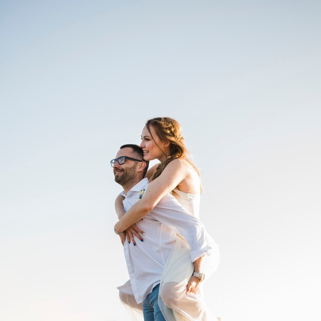 Man carrying his girlfriend on his back at a beach against blue sky