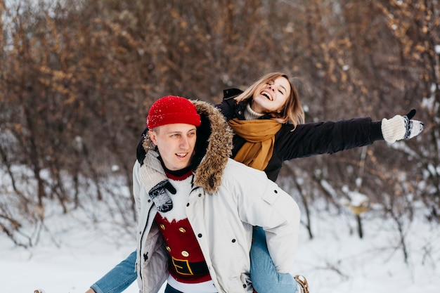 Man carrying woman on back in winter forest 