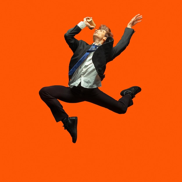 Man in casual office style clothes jumping and dancing isolated on bright orange