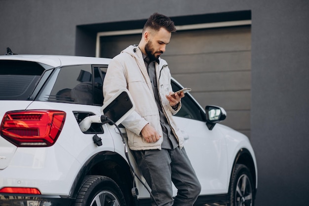 Man charging electric car by the house