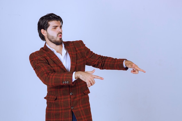 Man in checked blazer pointing at something in the right and talking about it.