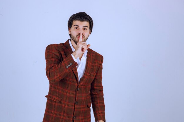 Man in checked jacket asking silence by showing his mouth.