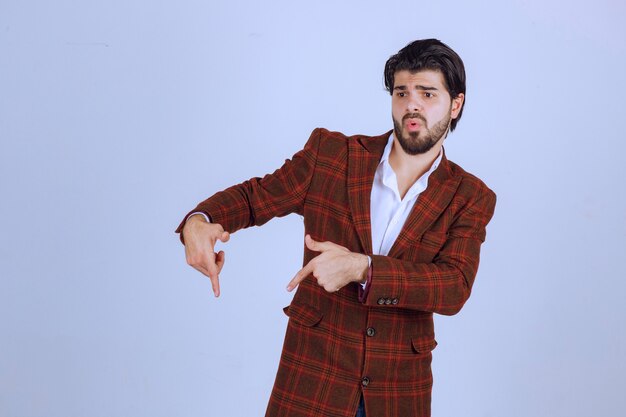 Man in checked jacket pointing down with finger and showing something.