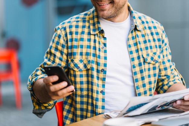 Человек в клетчатой ​​рубашке со смартфоном и газетой