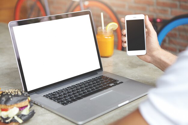 전자 장치에서 고속 인터넷 연결을 사용하여 전자 메일을 확인하는 사람. 열린 노트북 앞에 앉아 그의 손에 스마트 폰으로 남성