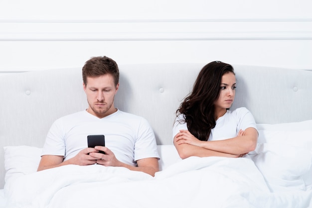 Foto gratuita uomo che controlla il suo telefono accanto alla sua ragazza arrabbiata