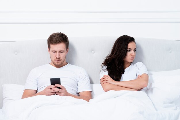 Man checking his phone next to his angry girlfriend