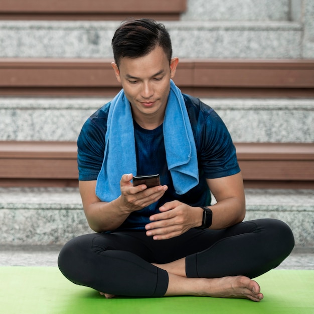 Человек проверяет свой смартфон после тренировки йоги