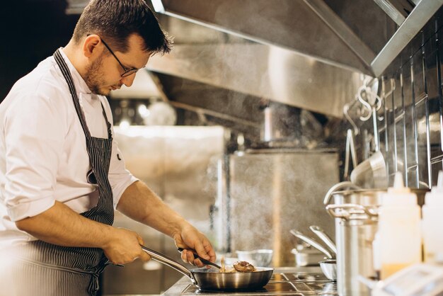 Man chef frying meat in a pan in fire