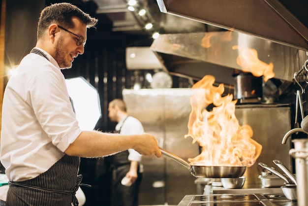 Free photo man chef frying meat in a pan in fire