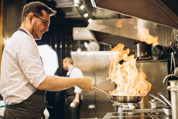 Man chef frying meat in a pan in fire