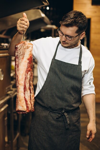 レストランの厨房で肉の大部分を握っている男のシェフ