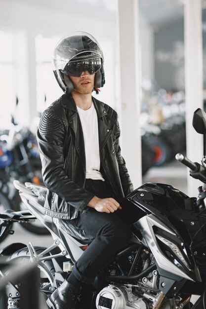 남자는 모토 가게에서 오토바이를 선택했습니다. 검은 재킷을 입은 남자. 헬멧에 남자입니다.