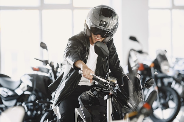 남자는 모토 가게에서 오토바이를 선택했습니다. 검은 재킷을 입은 남자. 헬멧에 남자입니다.