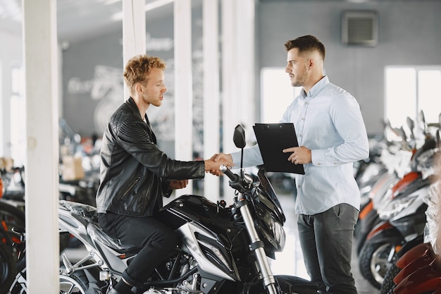 男はモトショップでバイクを選びました。黒のジャケットを着た男。クライアントとマネージャー。