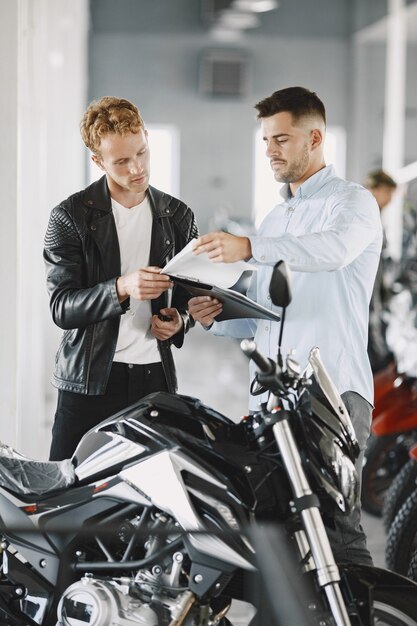 Man choosed motorcycles in moto shop. Guy in a black jacket. Manager with client.