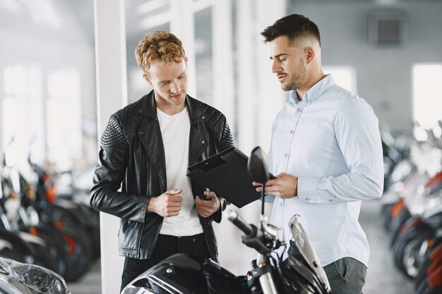 Man choosed motorcycles in moto shop. Guy in a black jacket. Manager with client.