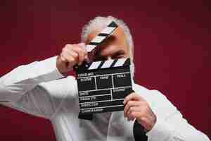 Free photo man in classic style shirt holds clapper white haired funny guy with beard in light clothes posing on burgundy background