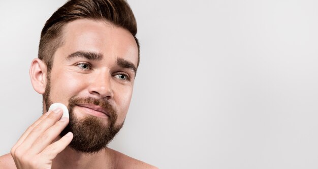 Man cleaning his face with a cleansing disk with copy space