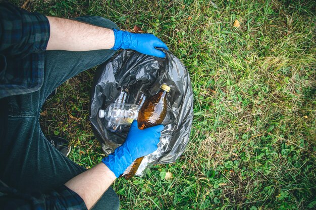 A man cleans up the forest throws a bottle into a trash bag closeup