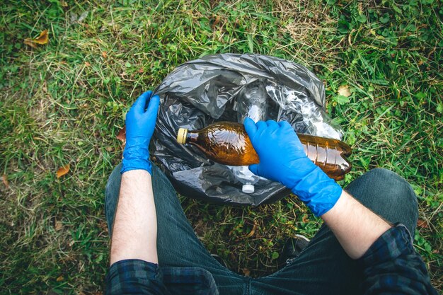 A man cleans up the forest throws a bottle into a trash bag closeup