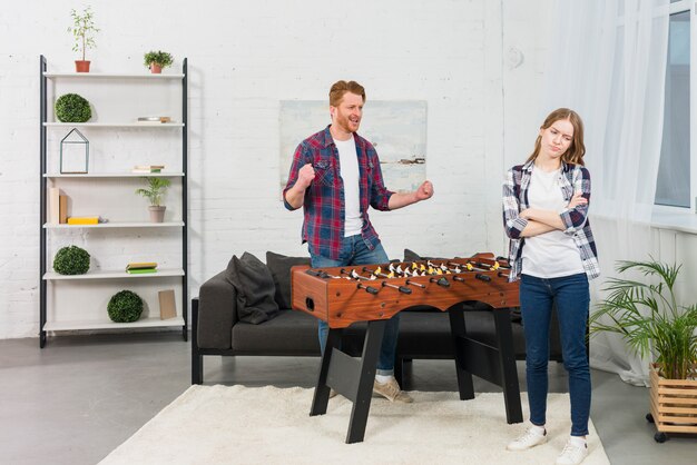 Man clenching her fist with joy looking at sad woman in the modern living room