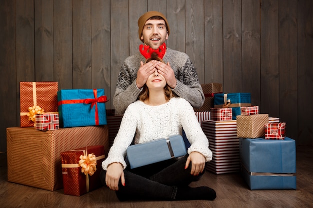 Man close his girlfriend's eyes with hands over wooden wall