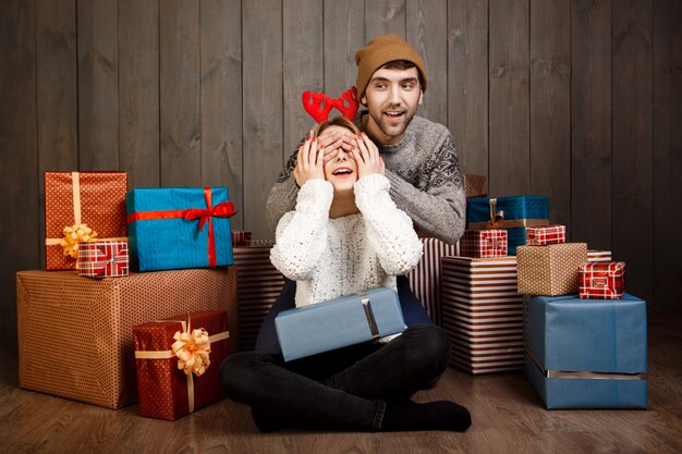 Man close his girlfriend's eyes with hands over wooden wall