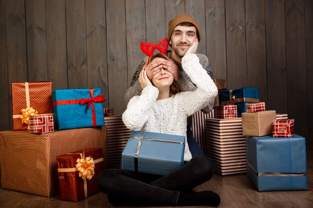 Man close his girlfriend's eyes with hands over wooden wall