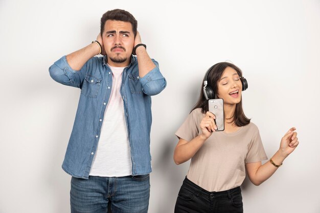 Man closing his ears while woman singing her heart out.