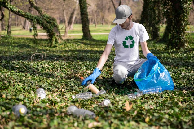 Мужчина собирает пластиковый мусор в загрязненном парке
