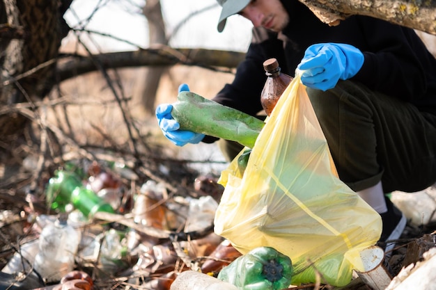 Мужчина собирает с земли разбросанные пластиковые бутылки