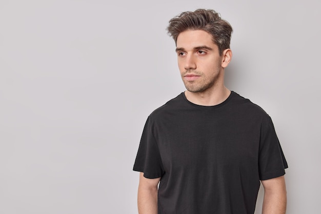 man concentrated away has deep thoughts dressed in casual black t shirt poses on white with copy space