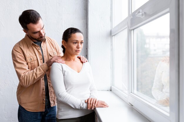 Man consoling sad woman at a group therapy session while looking through the window