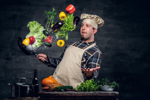 男の料理人は、野菜が空を飛んでいる鍋を持っています。