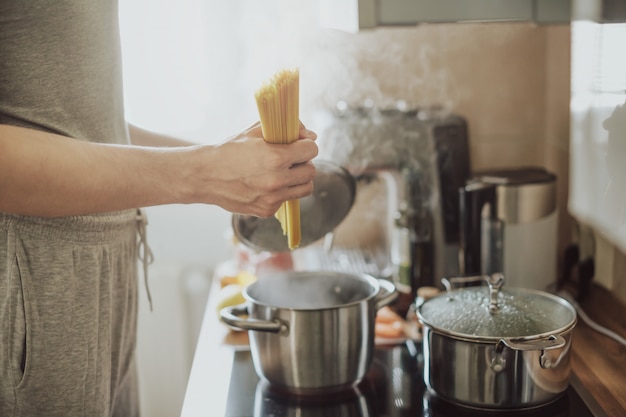 Man cooking pasta spaghetti at home in the kitchen. Home cooking or italian cooking concept.