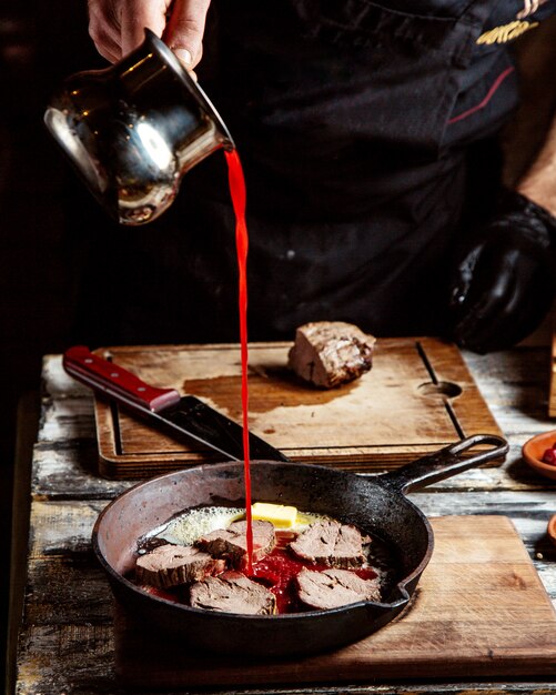  a man cooks fried meat in a pan and pour tomato juice