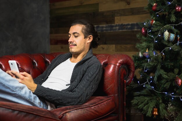 Человек на диване со смартфоном на Рождество