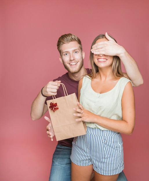 Free photo man covering her girlfriends eyes while giving gift shopping bag