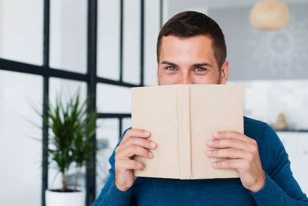 Man covering his face with book at home