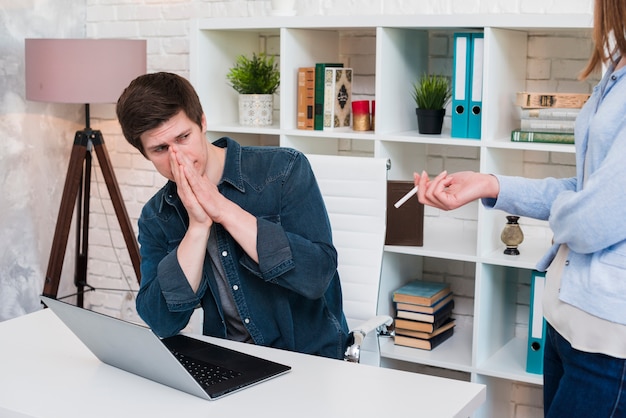 Man covering nose while his colleagues smoking in office