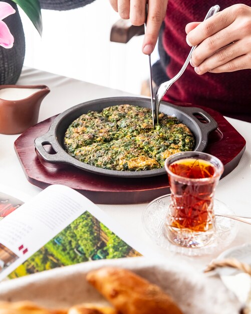 Man cuts kuku egg with herbs tea side view