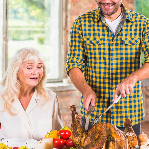 Man cutting baked chicken at table near amazed woman 