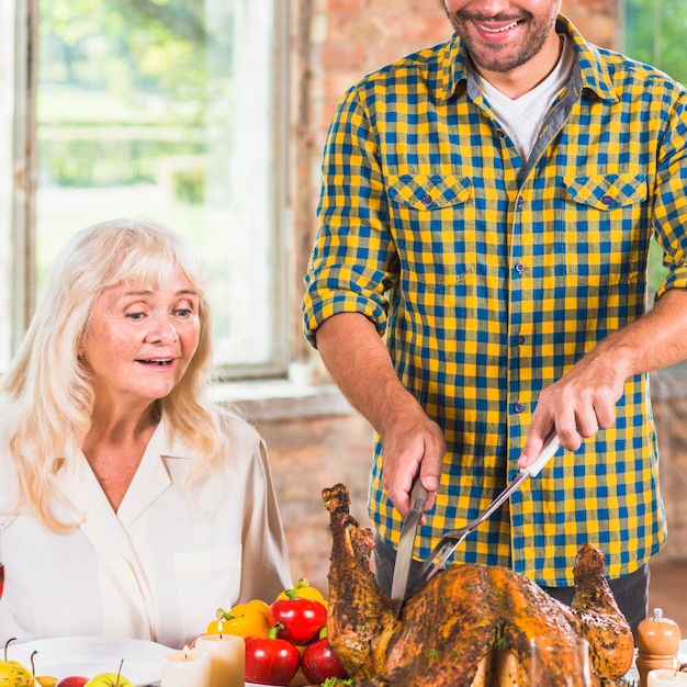 Man cutting baked chicken at table near amazed woman 