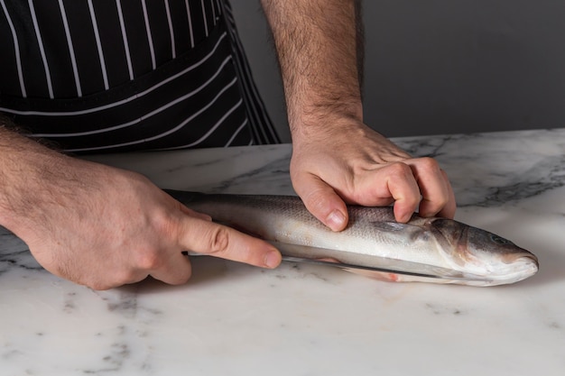 Free photo man cutting a bass fish for cooking