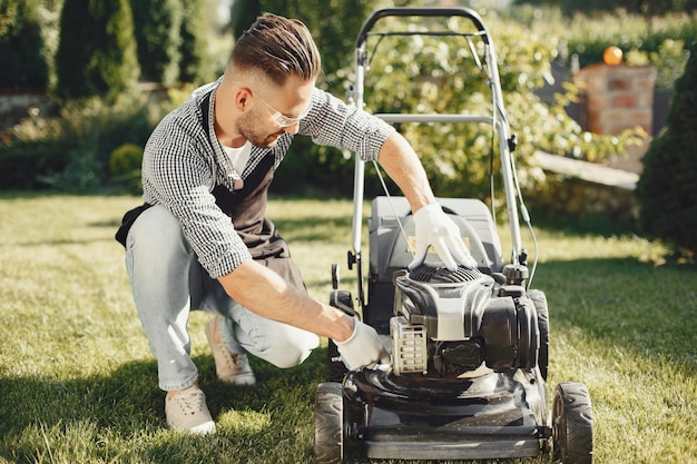 Man cutting grass with lawn mover in the back yard. Male in a black apron. Guy repairs.