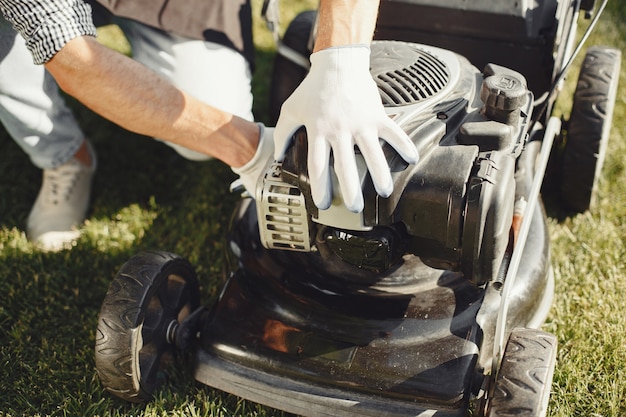 Man cutting grass with lawn mover in the back yard. Male in a black apron. Guy repairs.