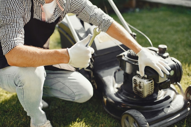 Man cutting grass with lawn mover in the back yard. Male in a black apron. Guy repairs.