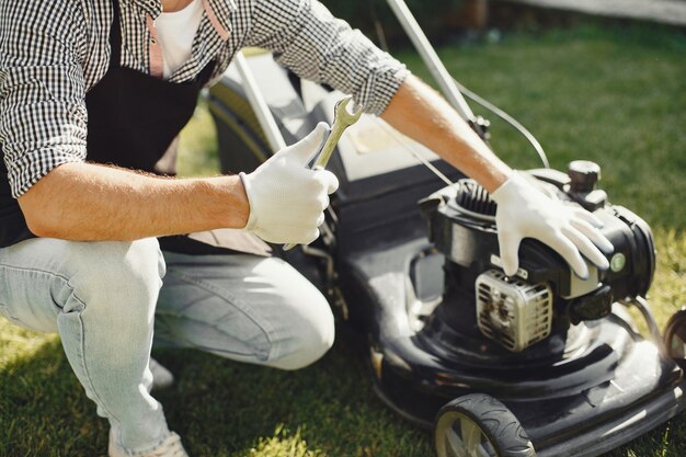 裏庭で芝刈り機で草を刈る男。黒いエプロンの男性。男は修理します。